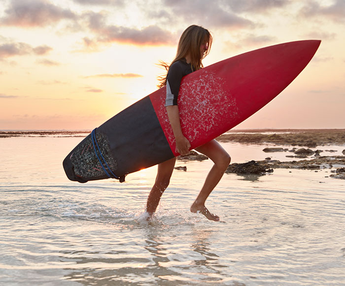 Mujer saliendo del mar con una tabla de Surf | Beneficios MP