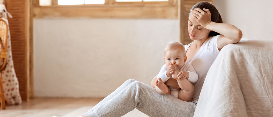 Mujer angustiada sentada en el piso con un bebé en brazos - La salud mental en la maternidad