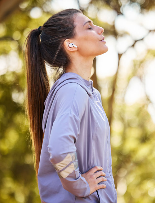 Mujer parada en un parque con la cara al sol | ¿Qué es el ejercicio de bajo impacto?