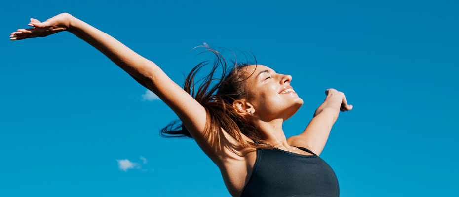 Mujer con los brazos abiertos hacia el sol, con un cielo celeste de fondo | Salud hormonal en la mujer